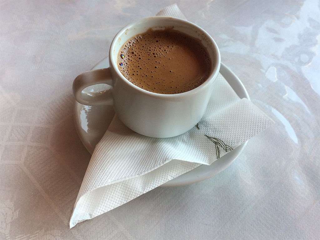 Greek coffee with frothy top served in a small white cup and saucer placed on the table.