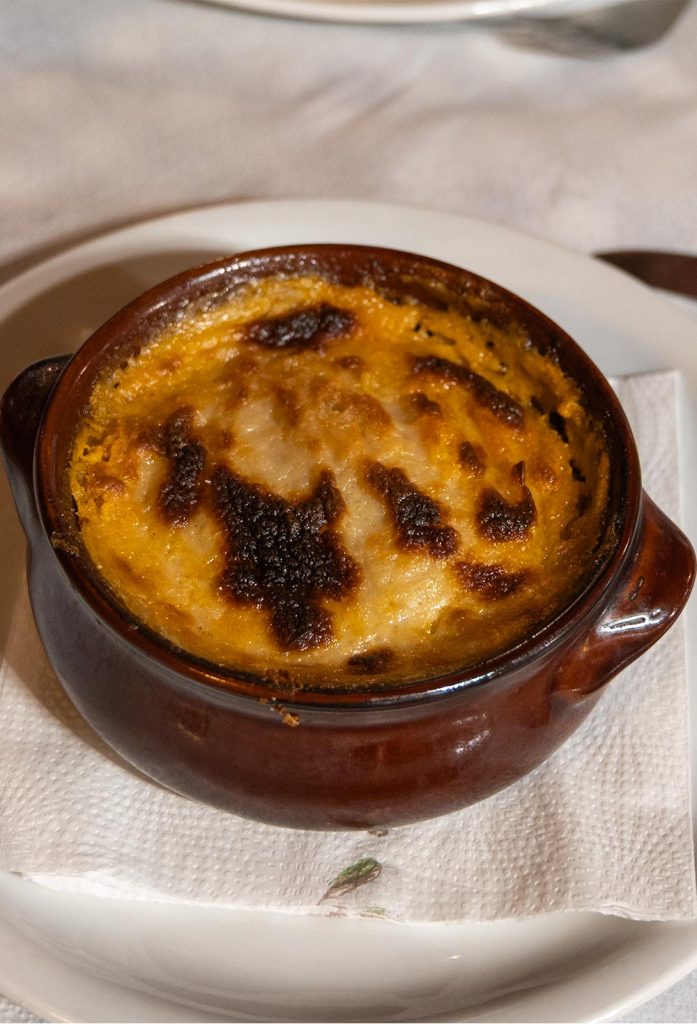 Award-winning meat and vegetable meal, with a golden béchamel crust in a round, presented in brown glazed clay pot.