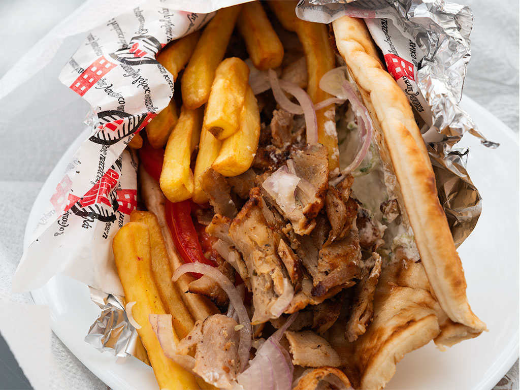 Pita Gyros. Cooked meat, sliced onions, tomatoes, creamy tzatziki and golden fries. Presented in a takeout bag.