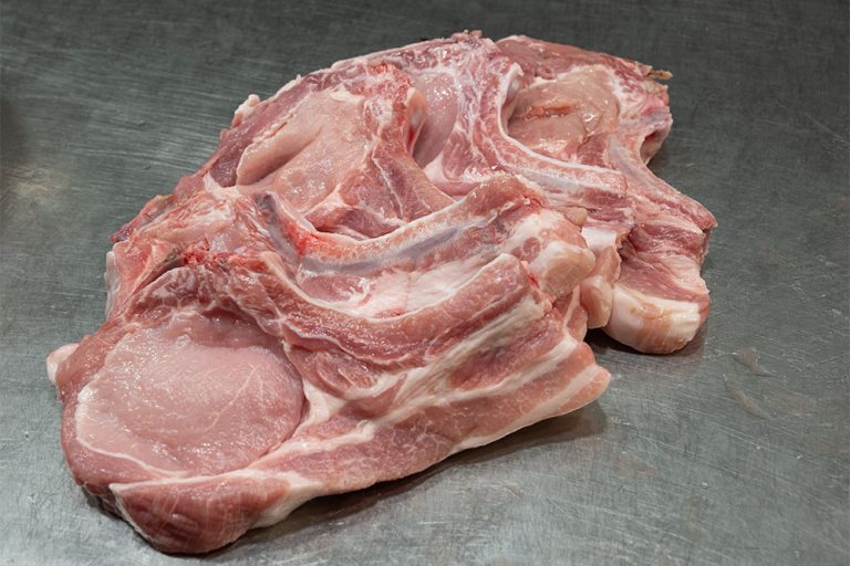 Five raw pork chops on the bone, displayed in a fan shape on a stainless steel kitchen counter.