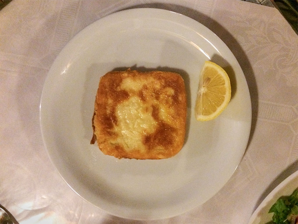 Cheese fried to a brown crust on a white plate and with a slice of lemon.