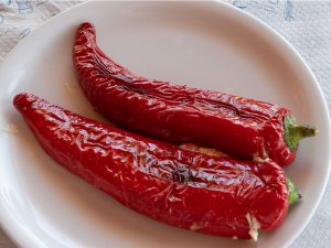 Two grilled sweet red long peppers, with a cheese filling and served on a white plate.
